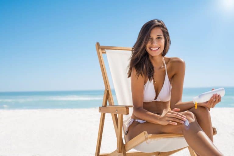 Laser Hair Removal Treatment Woman in swimsuit on beach chair at the beach smiling and applying lotion